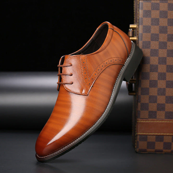 Scarpa elegante in pelle marrone lucida con dettagli traforati, suola nera, accanto a valigia a scacchi. Scarpe uomo formali, moda maschile.
