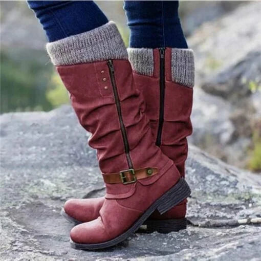 A close-up of a red orthopedic boot with a casual design and knitted cuff, worn by a person standing on rocky ground. The image highlights its stylish appearance and comfort features.